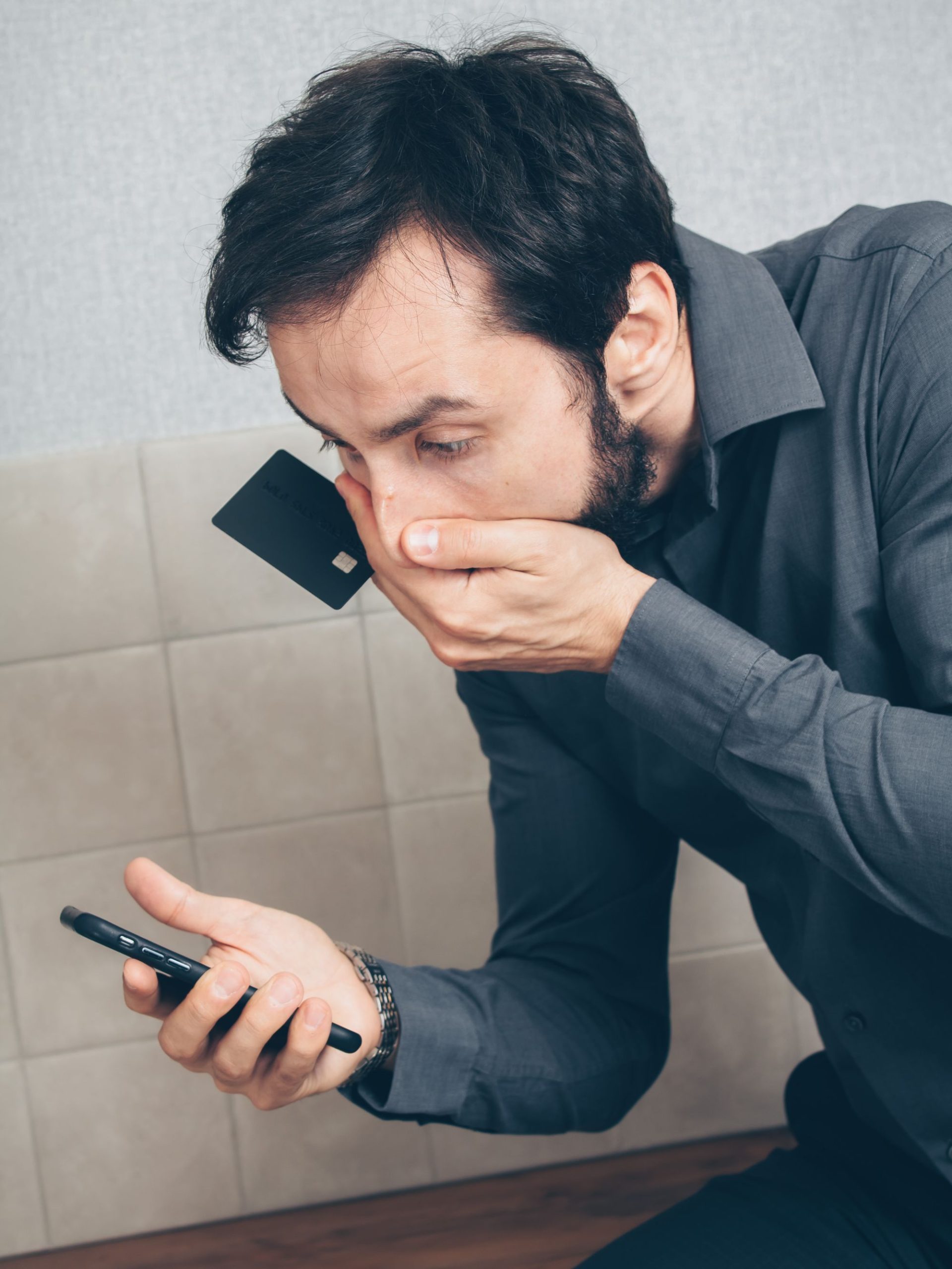 Muškarac zabrinut gleda u bankovnu karticu i telefon